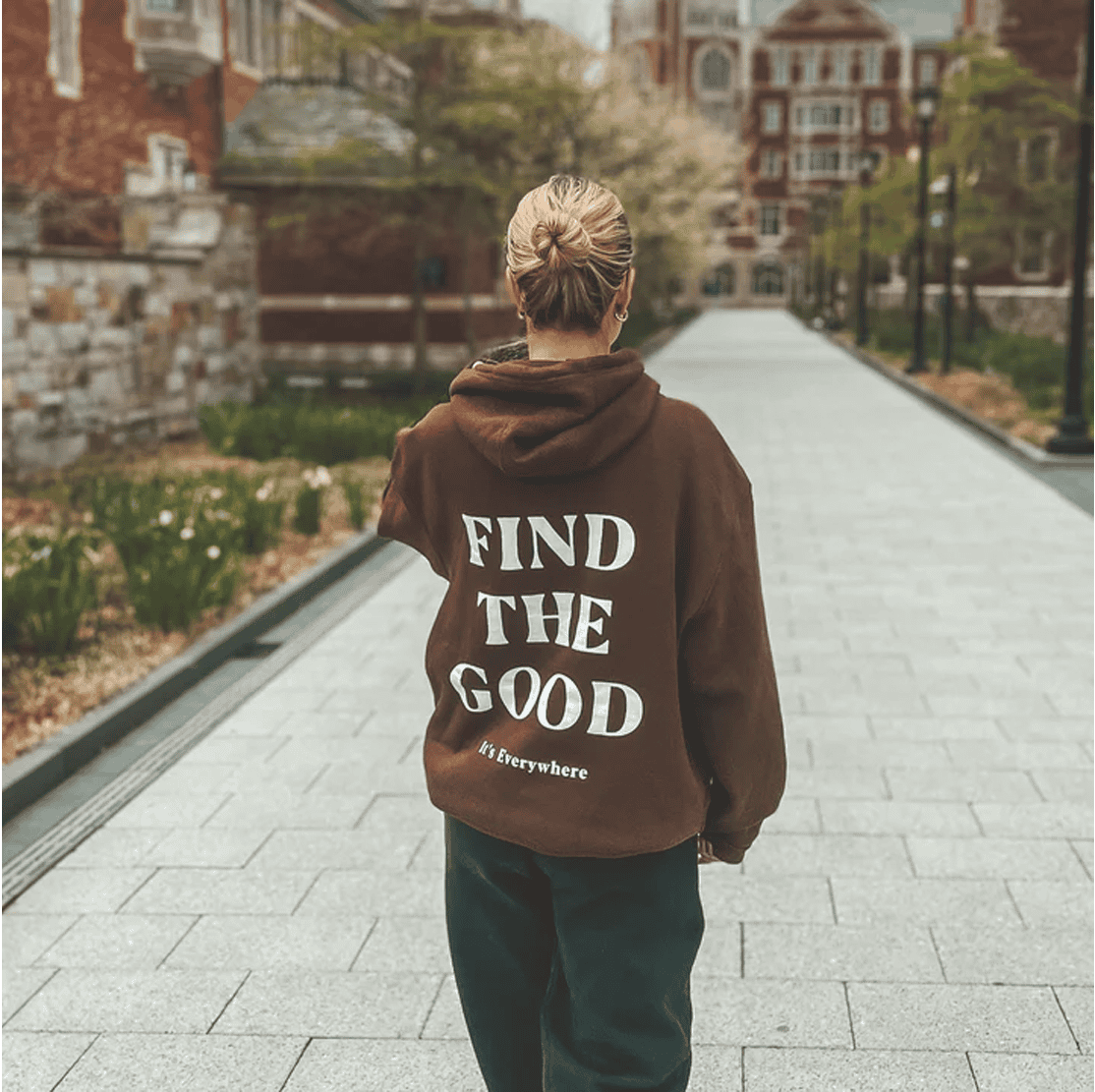 Woman standing outside in a mocha mousse sweatshirt that says "Find the Good"